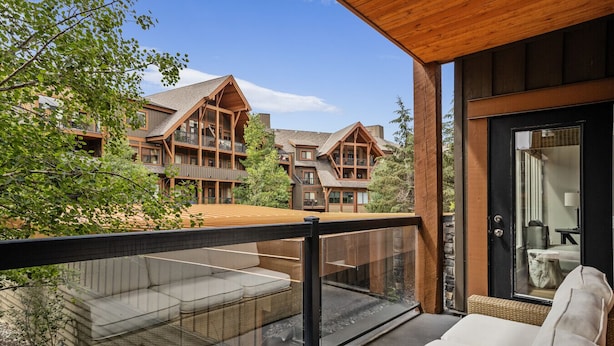 A balcony with a glass barrier, a wooden deck, and a view of a multi-story building with a wooden facade and large windows.