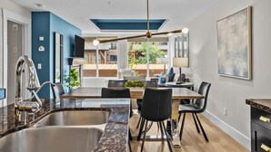 A modern kitchen with a central island, stainless steel sink, and a dining area with chairs and a table.