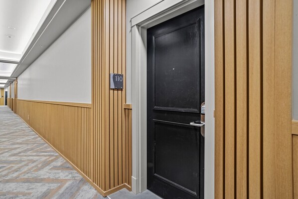 Pasillo de hotel con una puerta negra, un letrero con un número y un diseño de paneles de madera.
