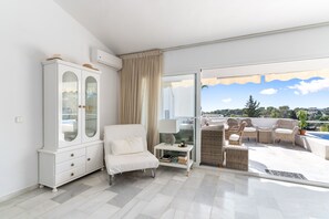 Ett modernt vardagsrum med en vit soffa, ett glasskåp och utsikt över en pool och grönområden.