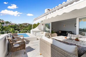 A rooftop terrace with outdoor furniture, a swimming pool, and a view of the surrounding landscape.