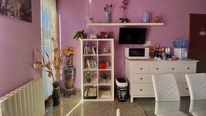 Un salón con una estantería blanca, un televisor, un microondas y una máquina de café.