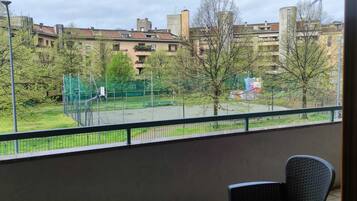 A balcony with a view of a tennis court, trees, and residential buildings.