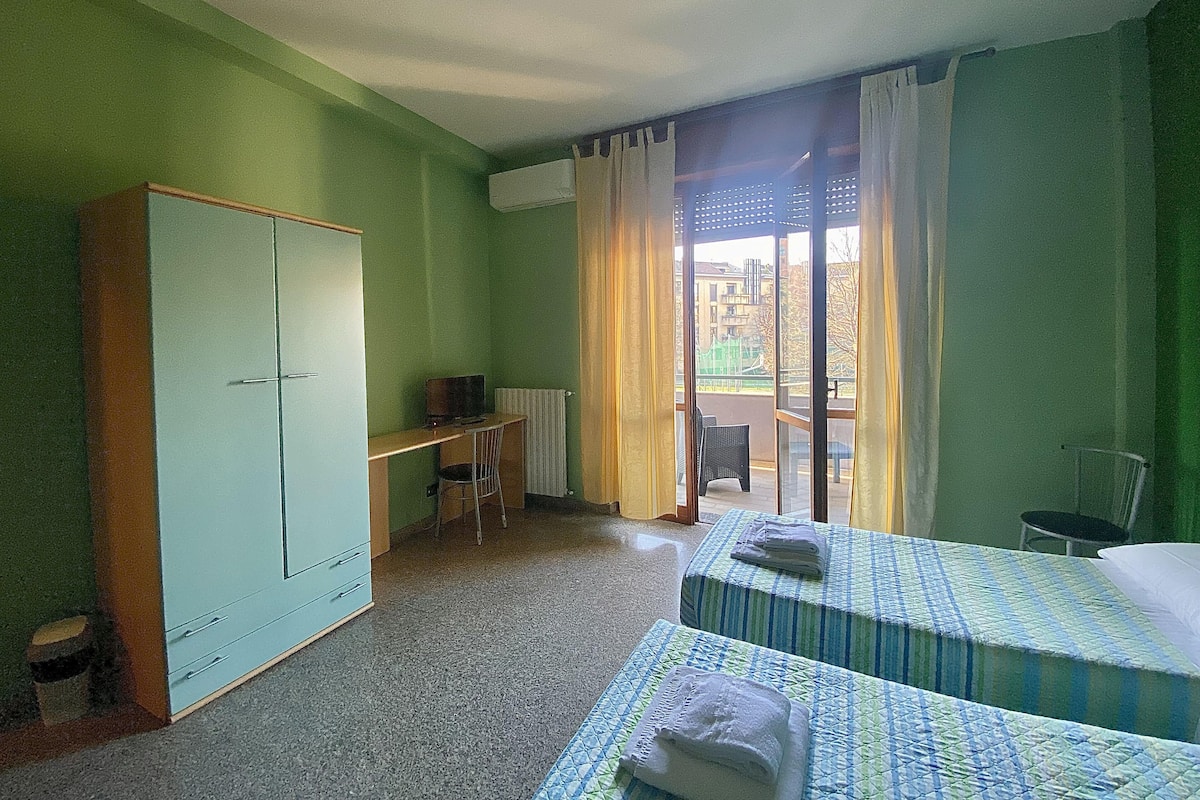A room with a wardrobe, a desk, a chair, and two beds with towels.