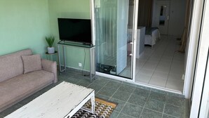 A living room with a sofa, a glass coffee table, a flat-screen TV on a glass stand, and a sliding glass door leading to a bedroom. - Villa Oasis Garden Apartment (Collectivity of Saint Martin)