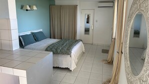 A bedroom with a bed, a large mirror, a door, and a window with curtains. - Villa Oasis Garden Apartment (Collectivity of Saint Martin)