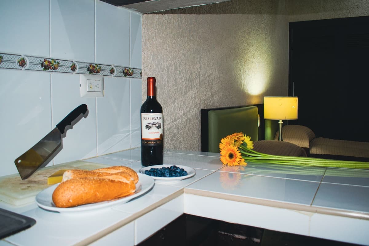 A kitchen counter with a loaf of bread, a bottle of wine, a knife, a bowl of blueberries, and a bouquet of sunflowers.