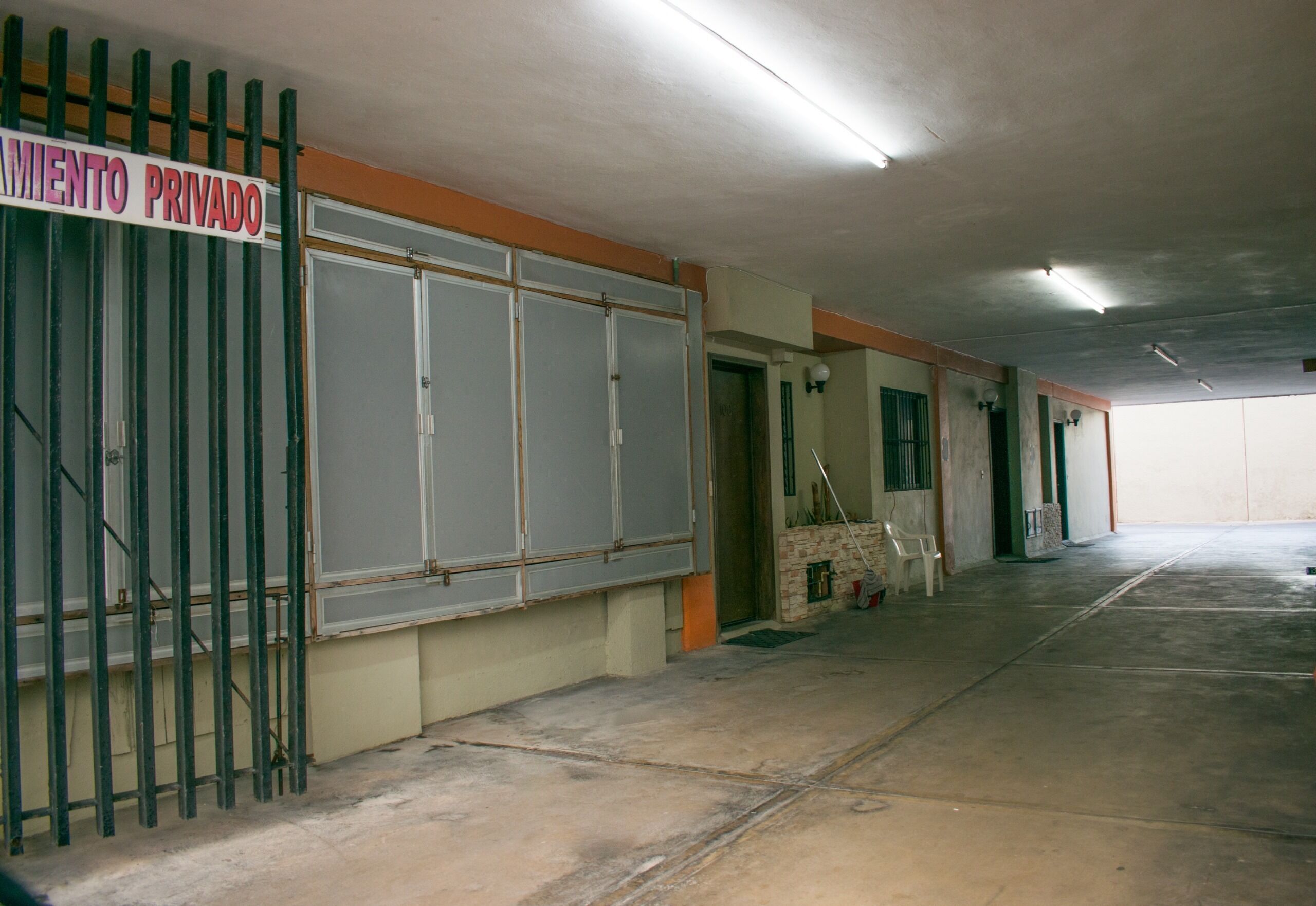 A private parking area with a gated entrance, concrete flooring, and a plain interior with a ceiling light.