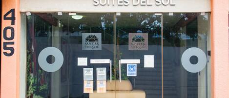 Entrada de um hotel com o nome "Suites del Sol" e um aviso indicando "De Volta ao Trabalho" e "Aberto".