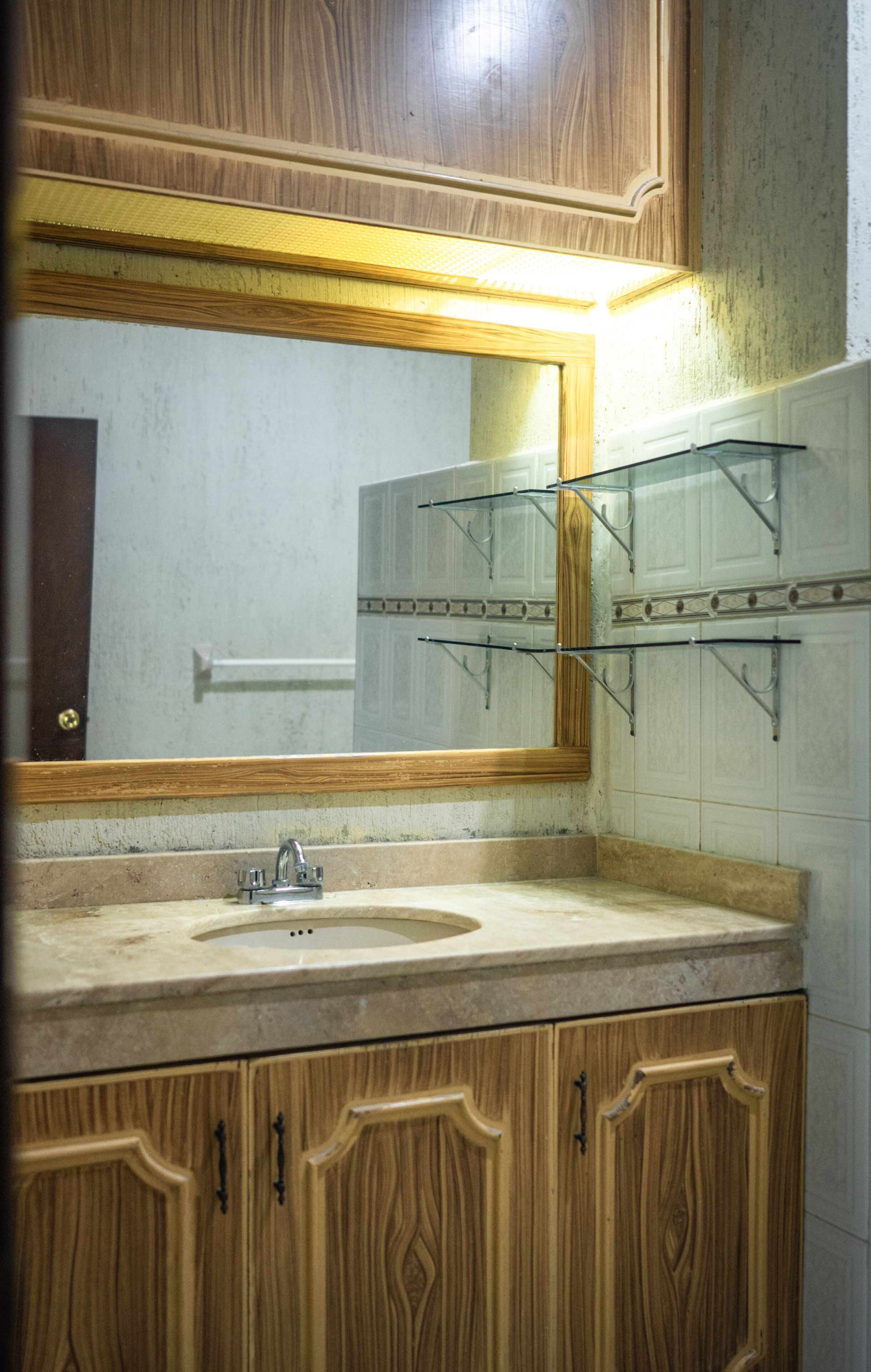 Une salle de bain avec des meubles en bois, un lavabo et un miroir surmonté d’une étagère.