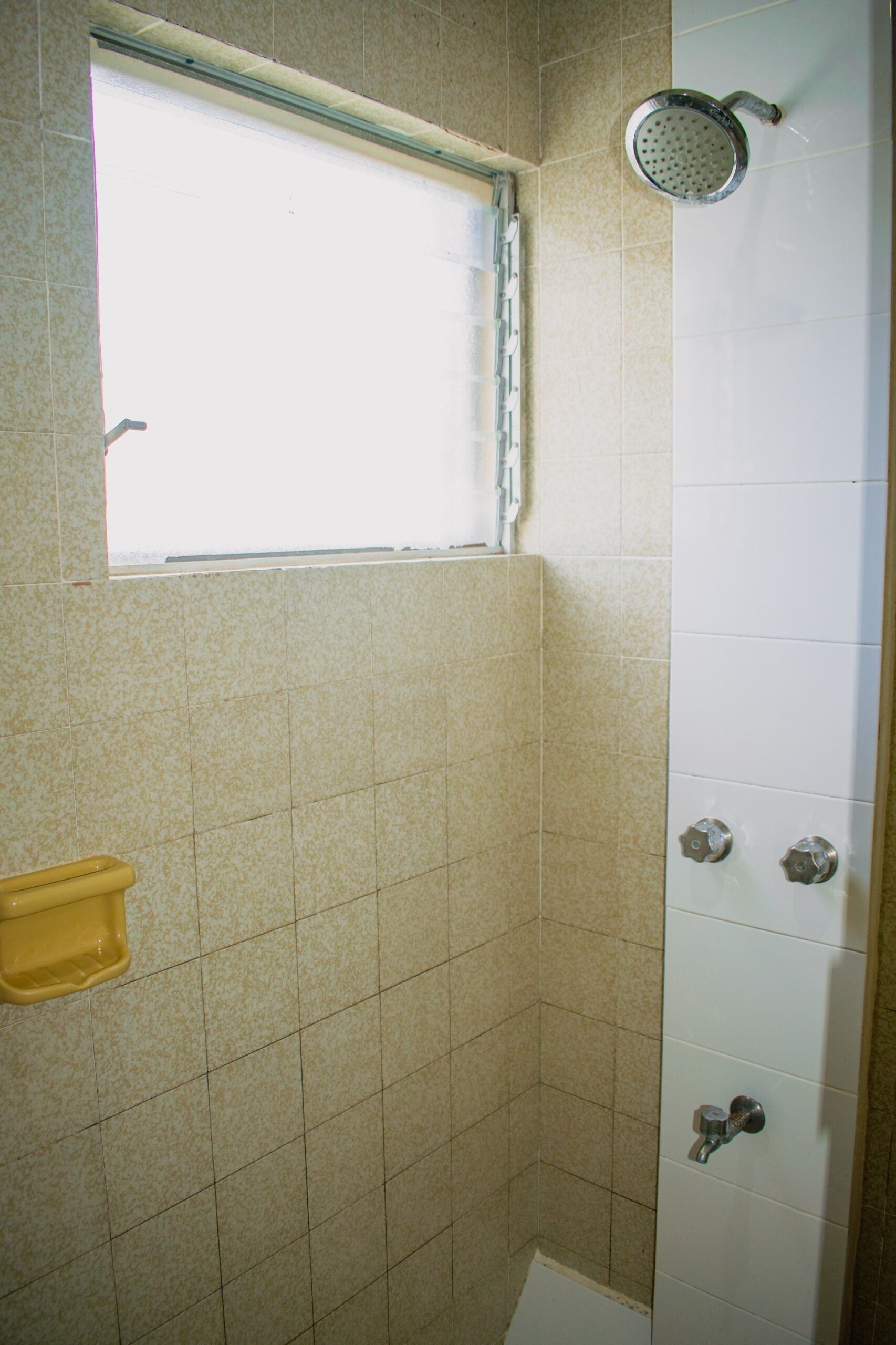 A small bathroom with a shower, a window, and a yellow soap dish.