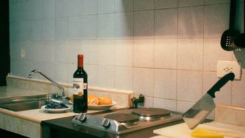 A kitchen with a sink, a wine bottle, a cutting board with a knife, and a plate with food.