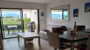 A modern living room with a dining area, large windows, and a view of the outdoors. - Grand T2, Centre Porticcio, 'tout à Pied', vue mer (Grosseto-Prugna)