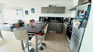 A modern kitchen with a dining area, stainless steel appliances, and a tiled floor. - Grand T2, Centre Porticcio, 'tout à Pied', vue mer (Grosseto-Prugna)