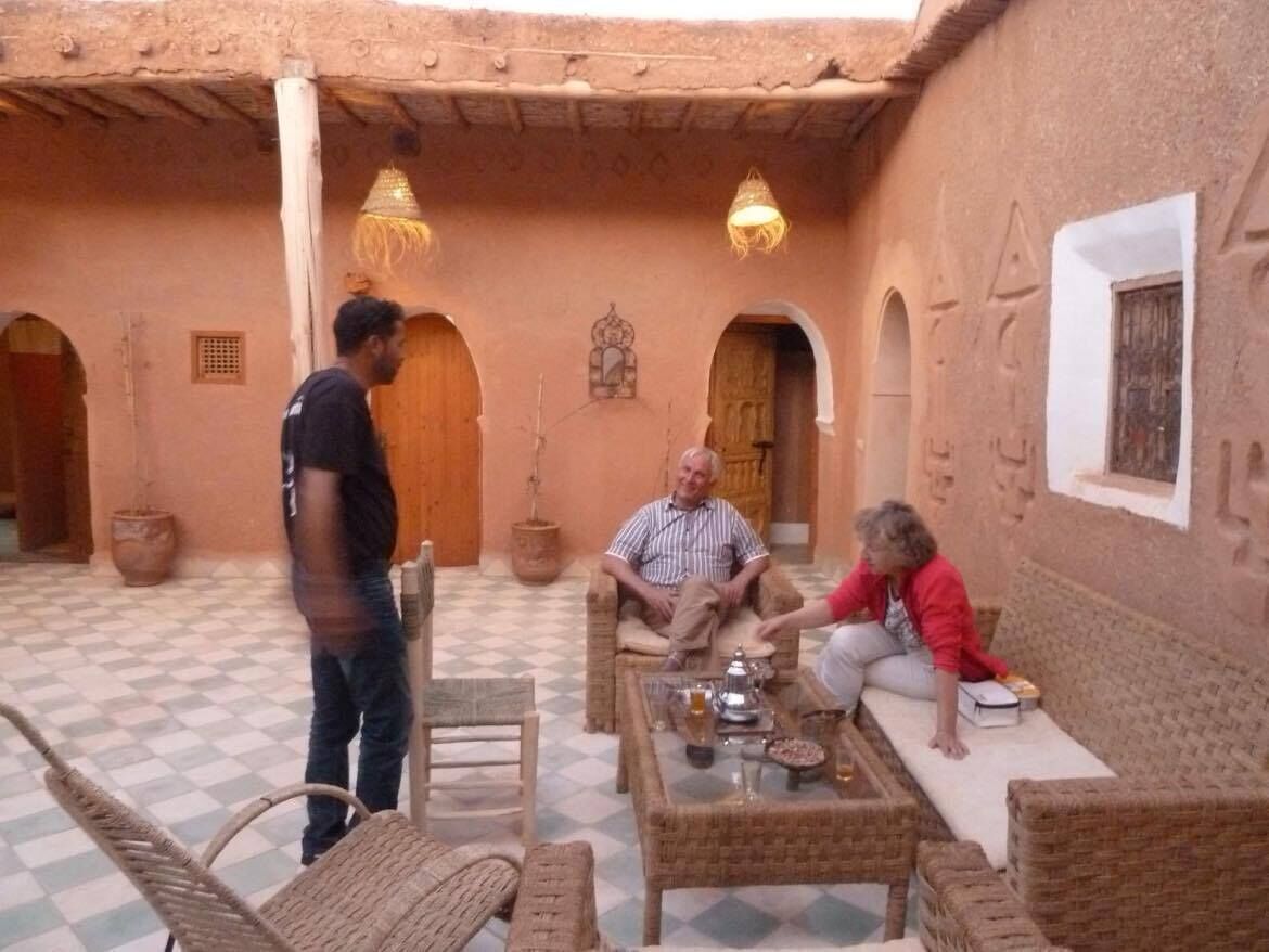 Een traditionele binnenplaats met een zwart-wit betegelde vloer, rieten meubels en een centrale tafel met een theepot en kopjes.
