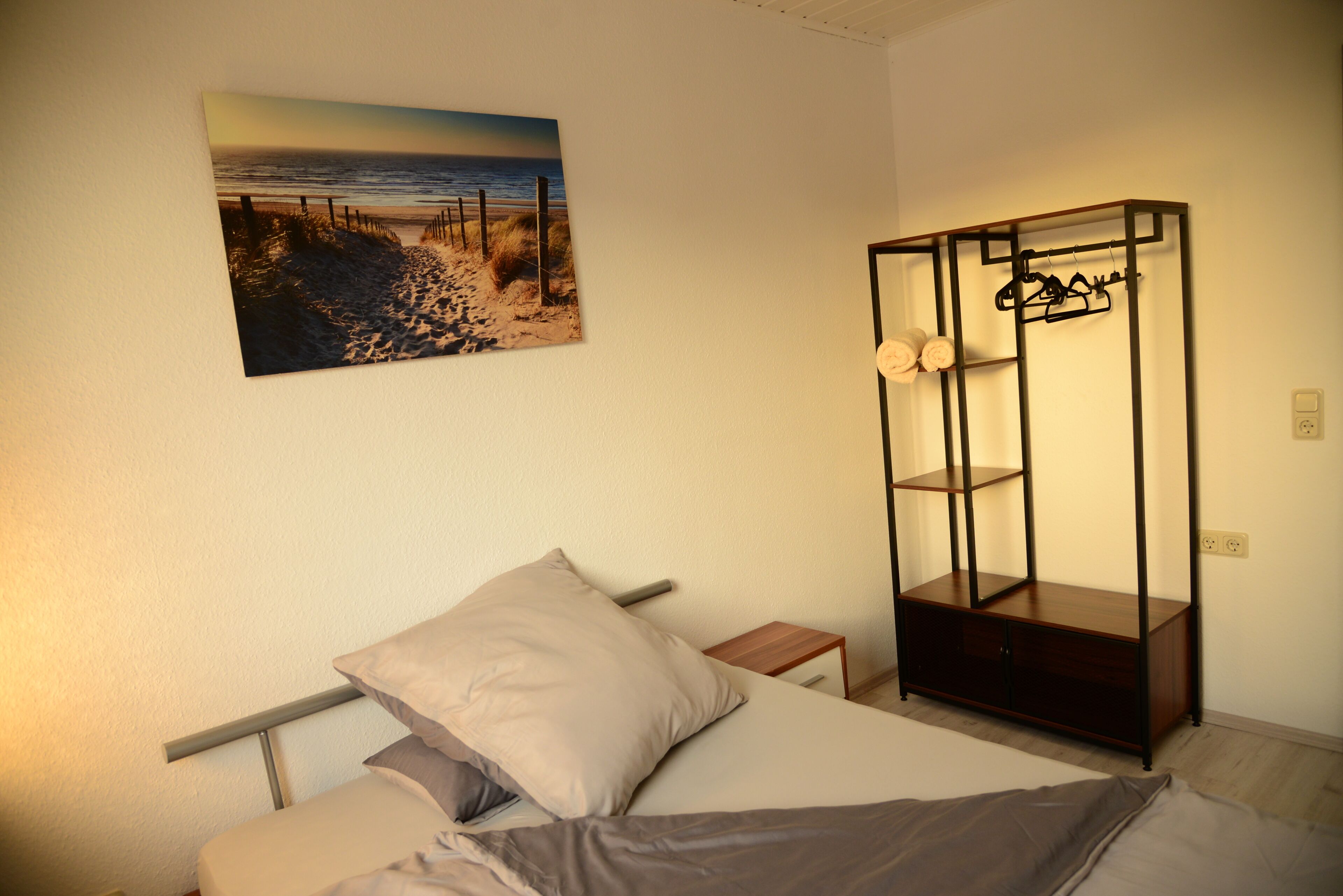 Ein Schlafzimmer mit Bett, Nachttisch, Holzschrank und Wanddeko im Strandhausstil.