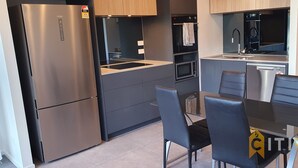 Une cuisine compacte équipée d’un réfrigérateur en acier inoxydable, d’un four à micro-ondes, d’un four et d’un évier. On y trouve une table à manger avec des chaises, ainsi qu’un petit îlot central doté d’un évier.