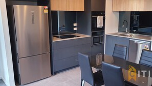 A modern kitchen with a stainless steel refrigerator, a built-in oven, and a microwave. There is a dining table with chairs and a small kitchen island with a sink. - Lovely in Lyneham - 1bd 1bth Apt (Lyneham)