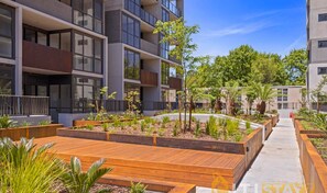 Un immeuble d’appartements moderne doté d’espaces de détente en plein air avec des sièges en bois et de jardins aménagés.