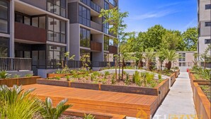 Un immeuble d’appartements moderne doté d’espaces de détente en plein air avec des sièges en bois et de jardins aménagés.