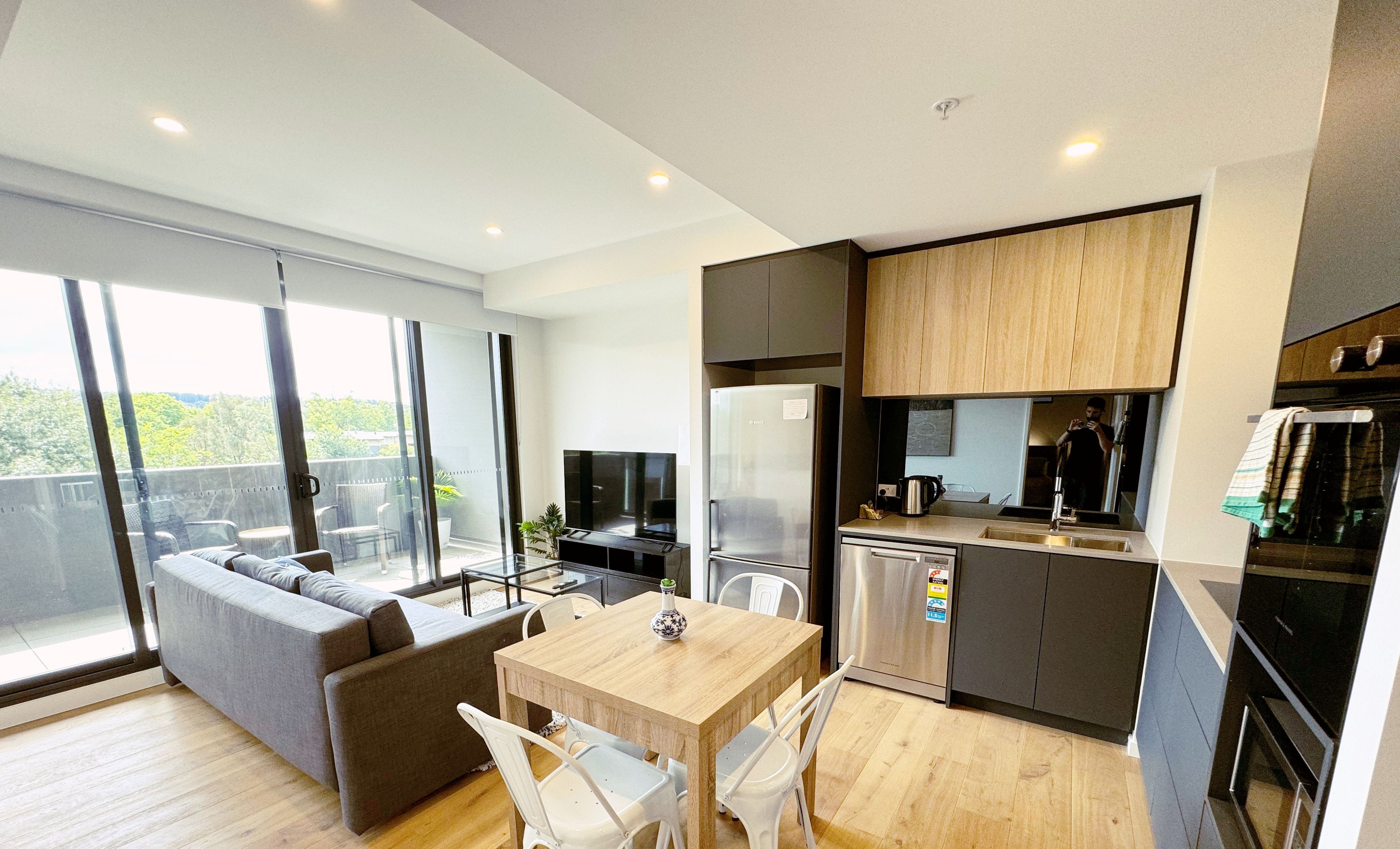 A modern apartment with a living area, dining space, kitchen, and a balcony with a view.