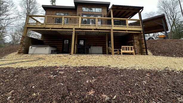 A two-story log cabin with a balcony, outdoor seating, and a stone fireplace. - Luxury cabin in county but not far from downtown. Hot tub on back porch.  (Ellijay)