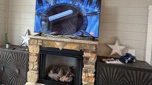 A fireplace with a stone mantle and a flat-screen TV mounted above it. - Luxury cabin in county but not far from downtown. Hot tub on back porch.  (Ellijay)