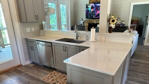 A modern kitchen with grey cabinets, a stainless steel dishwasher, a granite countertop, and a built-in oven. - Luxury cabin in county but not far from downtown. Hot tub on back porch.  (Ellijay)