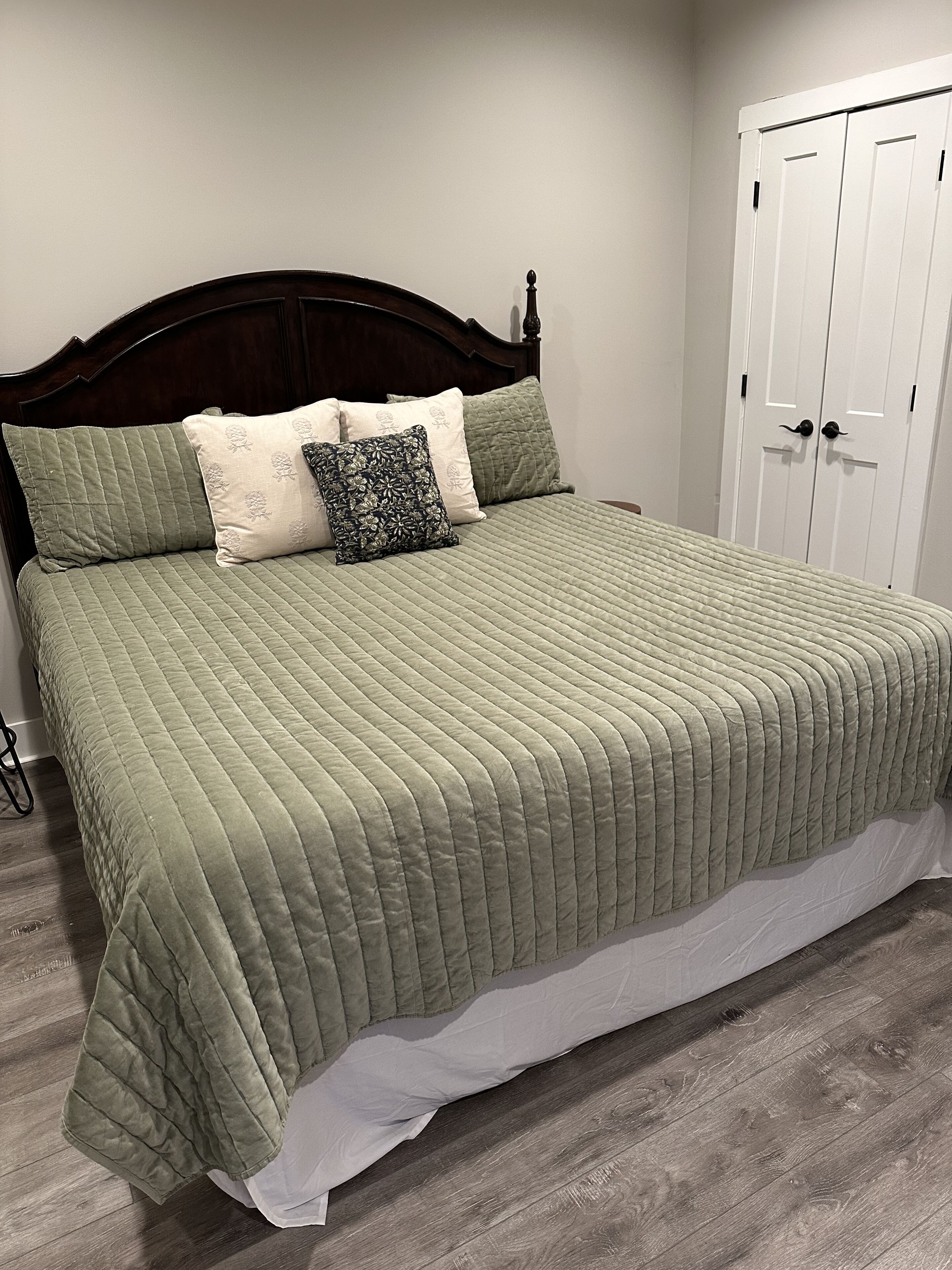 A neatly made bed with a green quilt, a dark wooden headboard, and a white door in the background.