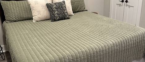 A neatly made bed with a green quilt, a dark wooden headboard, and a white door in the background.