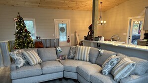 A cozy living room with a gray sectional sofa, a Christmas tree, and a wooden floor. - Luxury cabin in county but not far from downtown. Hot tub on back porch.  (Ellijay)