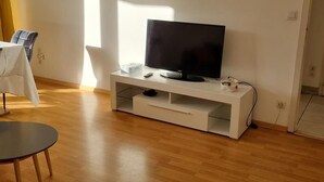 Ein modernes Wohnzimmer mit einem Flachbildfernseher auf einer weißen Unterhaltungseinheit, einem runden Esstisch und einem Sessel.