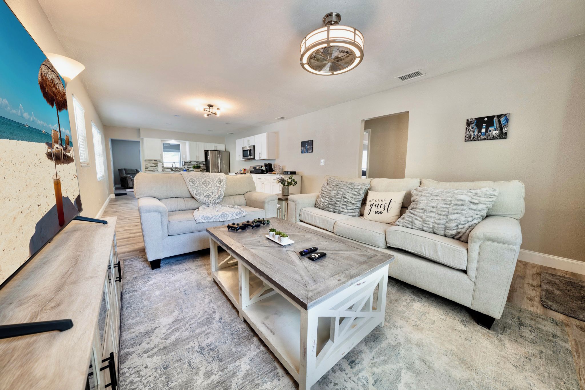 A spacious living room with a wooden coffee table, two sofas, a TV, and a kitchen in the background.