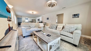 Ein geräumiges Wohnzimmer mit einem Couchtisch aus Holz, zwei Sofas, einem Fernseher und einer Küche im Hintergrund.
