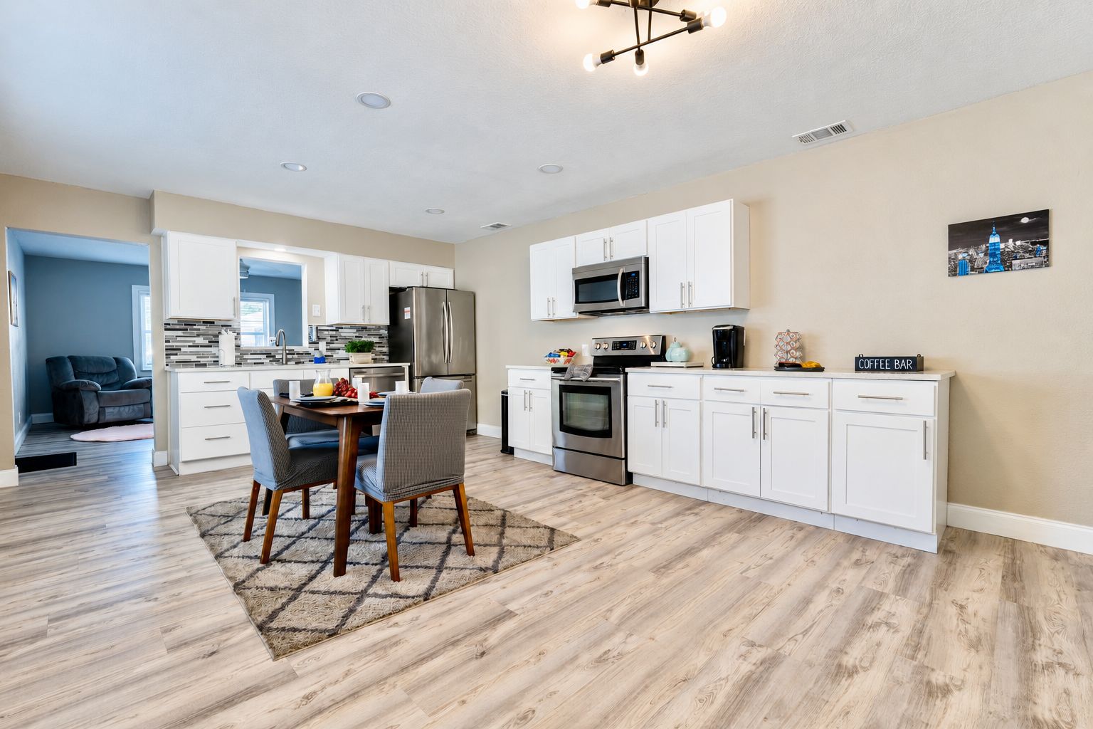 A modern kitchen with white cabinetry, a dining area with a table and chairs, and a microwave above the counter.