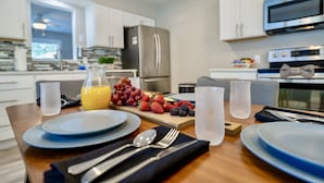 Eine moderne Küche mit weißen Schränken, Edelstahlgeräten und einem Essbereich, gedeckt mit Geschirr, Besteck und einer Obstplatte.