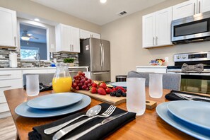 A modern kitchen with white cabinets, stainless steel appliances, and a dining area set for a meal with plates, cutlery, and fruit.