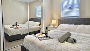 Ein Hotelzimmer mit großem Spiegel, einem Bett mit weißer Bettwäsche, einem Nachttisch mit Lampe und einem Fenster mit Jalousien.