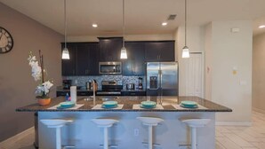 A modern kitchen with dark cabinets, stainless steel appliances, and a central island with bar stools. - Magical Townhome private pool in Storey Lake (Kissimmee)