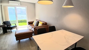 Un salon moderne avec un canapé, une table à manger et une vue sur une étendue d’eau, visible à travers une grande fenêtre.
