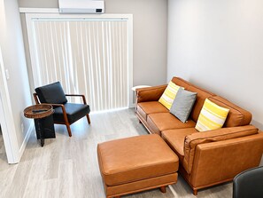Ein modernes Wohnzimmer mit einem braunen Ledersofa, einem schwarzen Sessel und einem kleinen Hocker.
