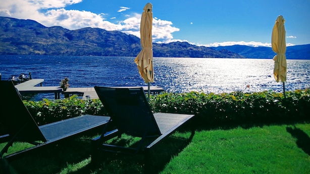 Un espace aménagé au bord de la piscine, avec des chaises longues et des parasols, offrant une vue sur un lac et des montagnes en arrière-plan.