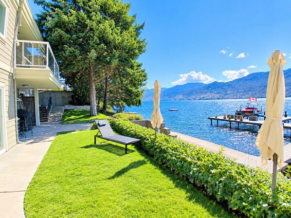 A well-maintained lawn with a lounge chair, a patio area with outdoor furniture, and a view of a lake with boats.