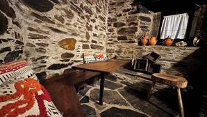 Un intérieur rustique en pierre, avec une table en bois, des bancs et un tapis à motifs.