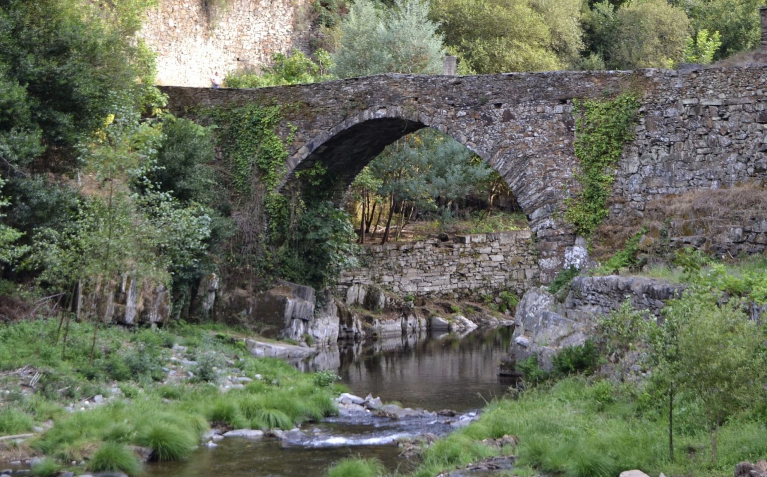 A stone bridge over a river with greenery on either side.