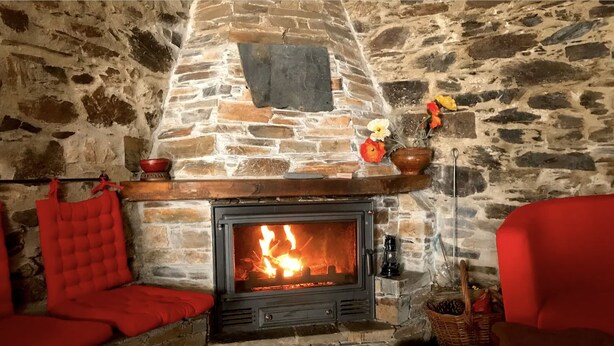 Une cheminée en pierre avec un feu de bois, un banc rembourré de coussins rouges et un fauteuil rouge.