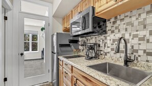Una cocina con armarios de madera, un lavamanos de acero inoxidable, un microondas y una cafetera.