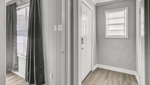 Un pasillo con una puerta, una ventana con persianas y un accesorio de iluminación.