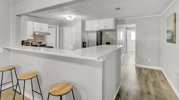 Una cocina moderna con armarios blancos, una isla central con taburetes y vista al área de comedor.