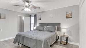 Un dormitorio con cama, ventilador de techo, mesita de noche y ventana con cortinas.